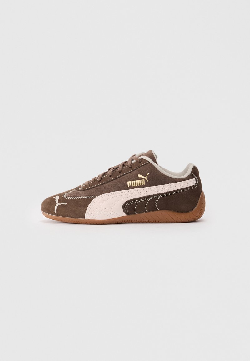 Brown suede athletic shoe with pink accents, featuring a curved leather side design, gold logo, and a textured rubber sole.