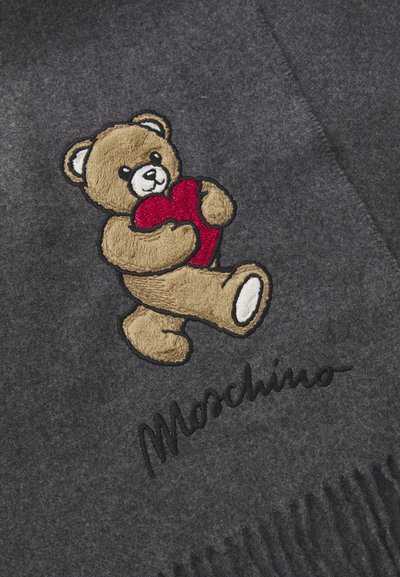 Harmaa villahuivi, jossa on brodeerattu karhu punaisen sydämen kanssa ja brändinimi "Moschino" mustalla käsialalla, sekä fringed yksityiskohtia.