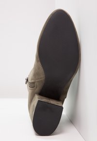 Botines de ante verde oliva con tacón cuadrado, cierre de cremallera lateral y suela de goma texturizada negra. Textura superior suave con detalles de costura.