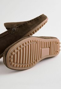 Braune Wildleder-Schlüpfschuhe mit einem weichen, strukturierten Obermaterial und einer beigen Gummisohle mit einem gemusterten Grip für Traktion.