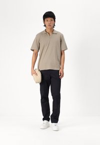 Khaki kortermet polo med tekstur, kombinert med marineblå bukser og hvite sneakers. Modellen holder en beige veske.