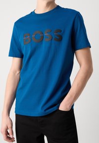 Camiseta de algodón azul con un gran logo negro de "BOSS" en el pecho. Manga corta, cuello redondo y un diseño de ajuste estándar.