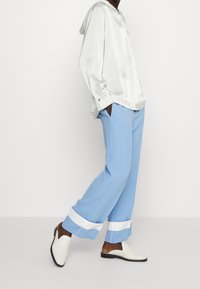 White satin button-up shirt, light blue wide-leg trousers with white cuffs, and white slip-on shoes. Smooth texture with a relaxed fit.