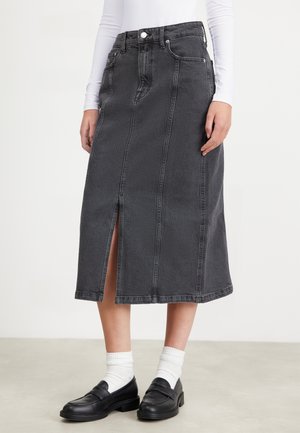 Jeanskjørt i mørkegrått med slits foran, strukturert passform, synlige sømmer og klassisk fem-lommers design. Brukt med sorte loafers og hvite sokker.
