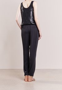 Top de tirantes negro con lentejuelas combinado con pantalones negros ajustados. Las sandalias cuentan con un detalle metálico. Tejido suave, corte relajado, con un diseño minimalista.