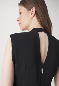 Black sleeveless dress featuring a V-back with a button closure and a side zipper, crafted from smooth fabric with a matte finish.