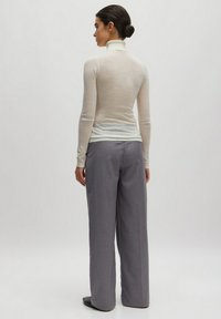 Enganliegendes, hellbeiges Rollkragenoberteil kombiniert mit lockeren, hoch taillierten grauen Hosen. Sanfte Texturen und minimalistisches Design.