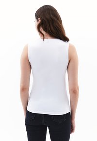 Witte mouwloze top gemaakt van glad materiaal, strak ontwerp, ronde hals en omgezoomde randen, gedragen met donkere jeans. Minimalistische stijl.