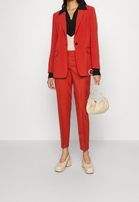Czerwona, dopasowana marynarka z dopasowanymi spodniami o wąskim kroju, czarny top oraz beżowe buty na platformie, uzupełnione kremową torebką.