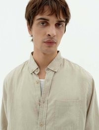 Helles beiges Hemd mit kurzer Kragenform, vertikalen Nahtdetails, Brusttasche und natürlicher Stoffstruktur.
