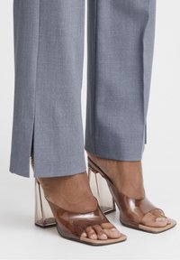 Pantalons gris sur mesure avec des fentes latérales, associés à des sandales à talons bloc transparentes avec une ouverture à l'avant et une finition lisse.