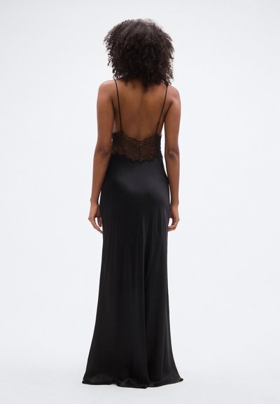 Μαύρο σατέν φόρεμα με δαντέλα στο πίσω μέρος, λεπτές ρυθμιζόμενες τιράντες και μακριά, ρέουσα φούστα. Λεία υφή, εφαρμοστή γραμμή.