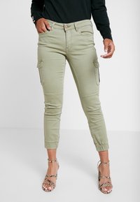 Ljusgröna cargobyxor med sidofickor, smala muddar och en slät yta. Bärs med strappy sandaler i neutrala nyanser.