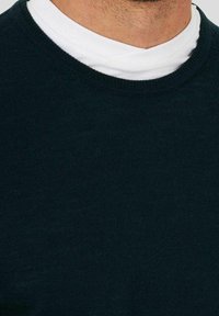 Donkergroen sweatshirt met een ronde hals en lange mouwen, met een zachte textuur en een gelaagd wit T-shirt eronder.