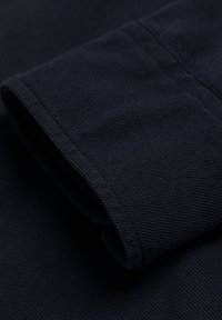 Acercamiento de una manga de tela de punto azul marino doblada que muestra la textura y las costuras en detalle.