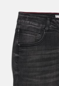 Schwarze Denim-Jeans mit glatter Textur, ausgestattet mit einer Vordertasche, Gürtelschlaufen und roten Nähten entlang des Taillenbunds.