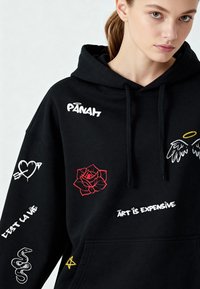 Felpa nera con cappuccio, dotata di grande tasca frontale, caratterizzata da vari ricami colorati, tra cui una rosa, cuori e testi.