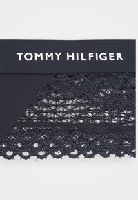 Navy blonde detaljer som vises med en glatt livlinje som har hvit "TOMMY HILFIGER" skrift; intrikate mønstre og teksturerte kanter synlige.