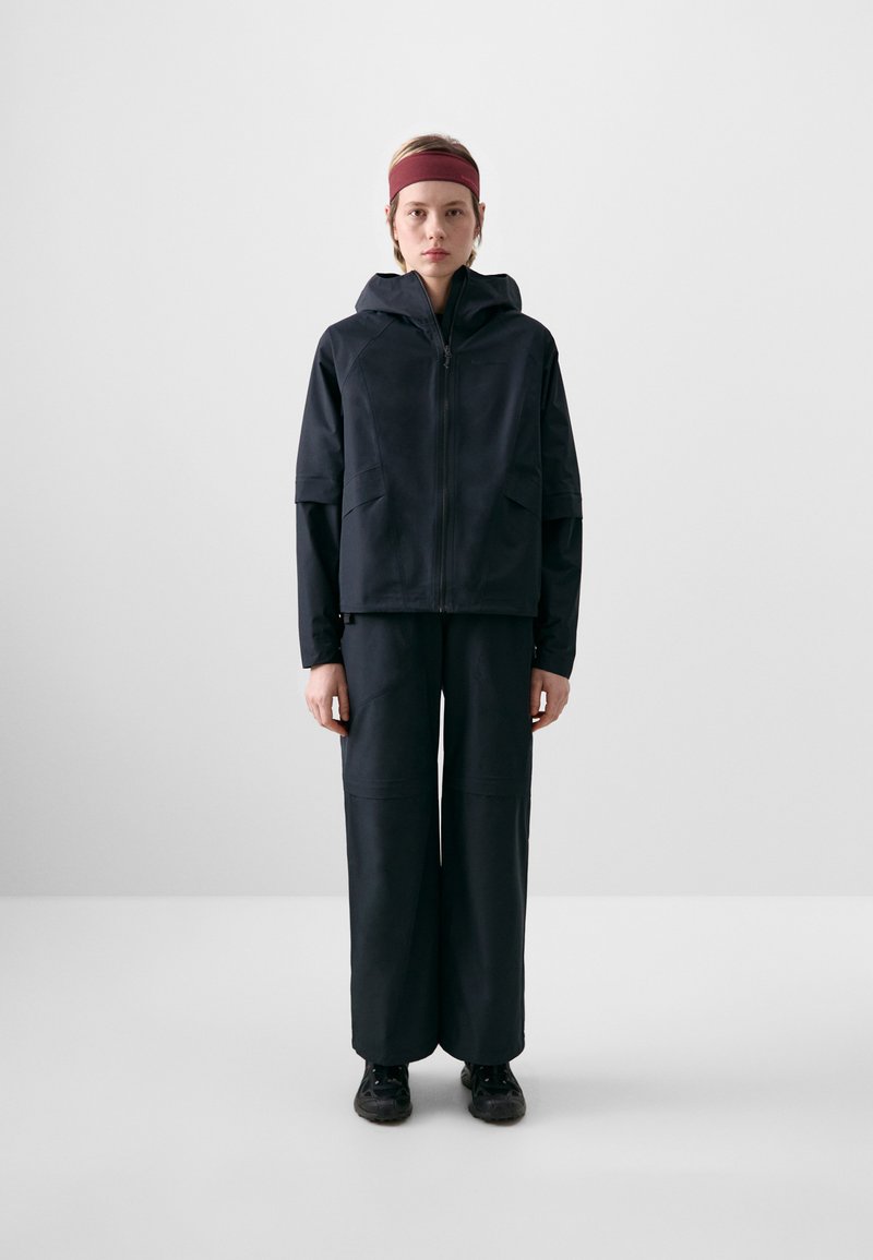 Black waterproof jacket with hood and zip, paired with loose-fitting black pants. Smooth texture, minimalistic design, and no visible logos.