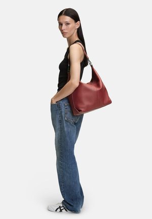 Rode leren hobo tas met een gestructureerde afwerking, slungelige vorm en een afneembare schouderriem, weergegeven tegen een plain witte achtergrond.