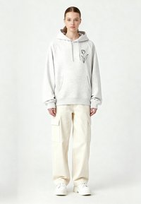Felpa con cappuccio grigia con motivo a tulipano, dotata di tasca a marsupio. Abbinata a pantaloni cargo color crema e sneakers bianche. Texture liscia.