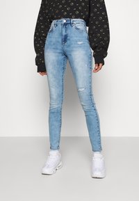 Jean skinny taille haute bleu clair avec des détails déchirés, doté d'un design classique à cinq poches et d'une fermeture éclair.