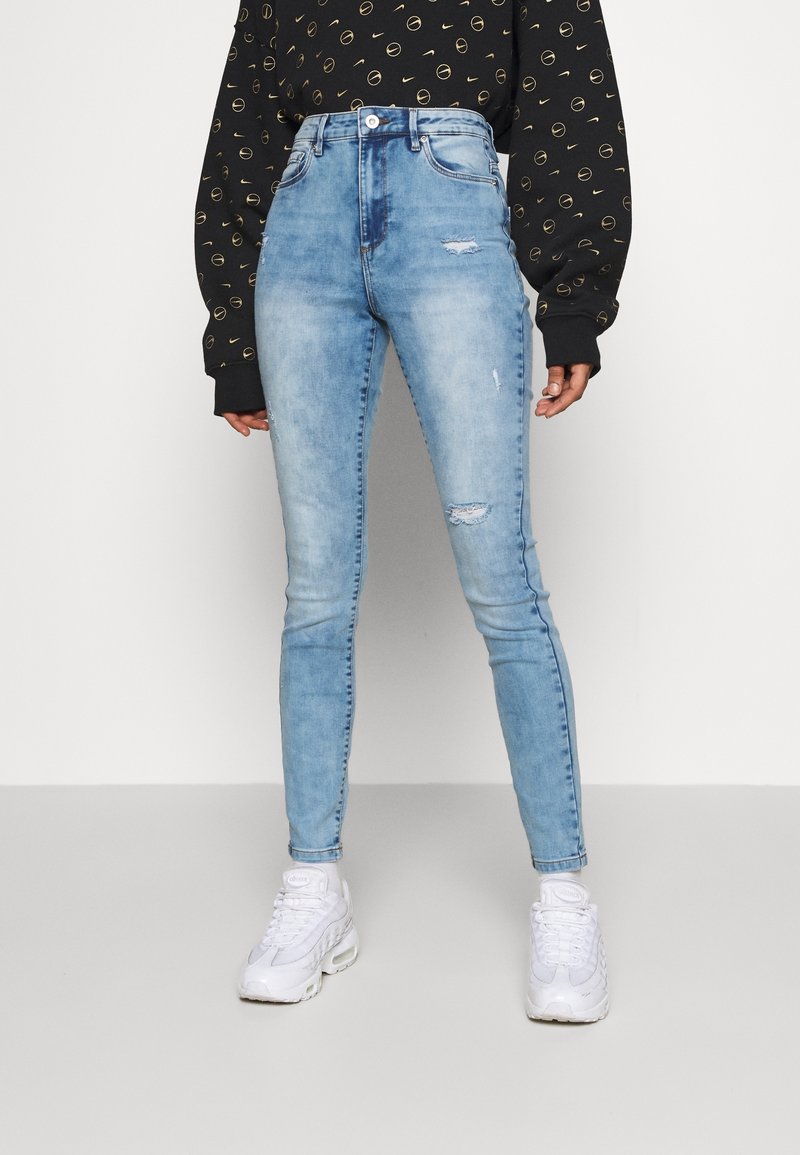 Jean skinny taille haute bleu clair avec des détails déchirés, doté d'un design classique à cinq poches et d'une fermeture éclair.
