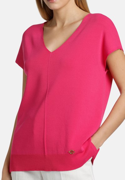 Bright pink short-sleeve V-neck top made of soft knit material, featuring a ribbed hem and a small logo accent at the bottom.
