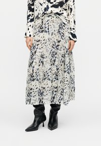 Μακριά φούστα από ελαφρύ ύφασμα με σχέδιο που περιλαμβάνει μαύρες και σκούρες μπλε πιτσιλιές σε λευκό φόντο, με τελείωμα από βαθμιδωτά βολάν.