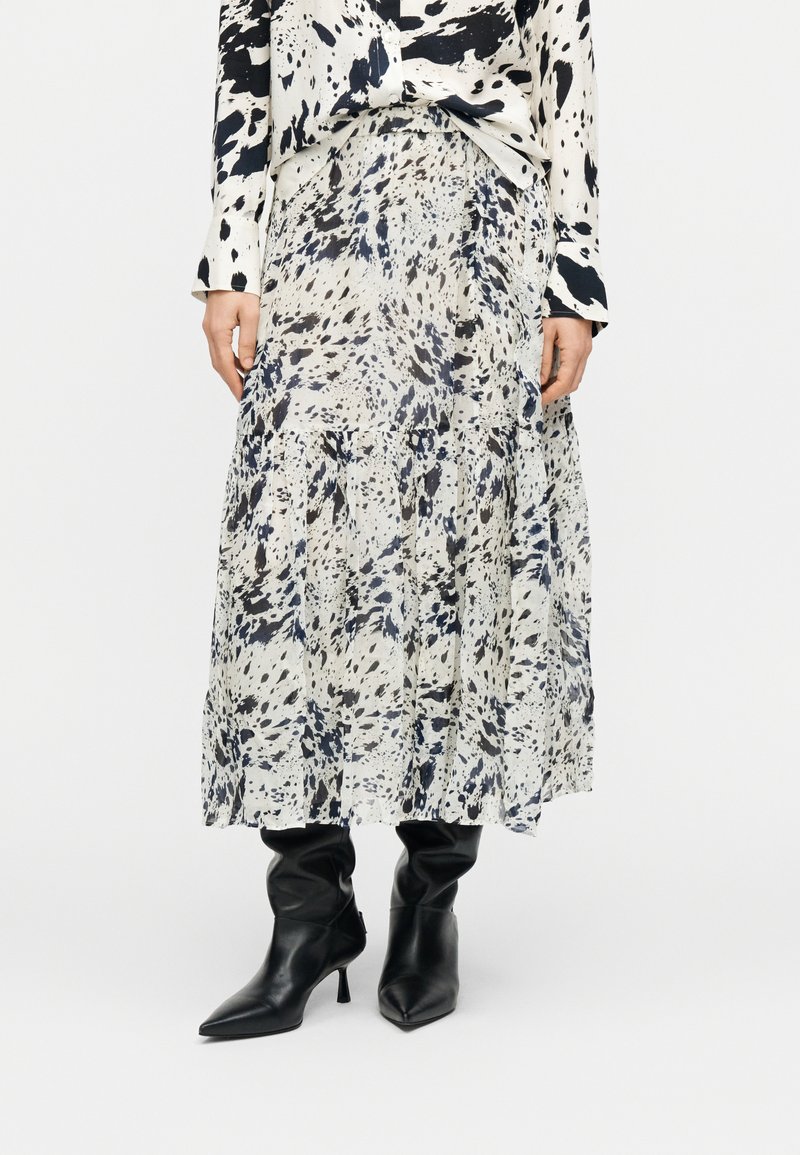 Μακριά φούστα από ελαφρύ ύφασμα με σχέδιο που περιλαμβάνει μαύρες και σκούρες μπλε πιτσιλιές σε λευκό φόντο, με τελείωμα από βαθμιδωτά βολάν.