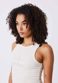 Light beige ribbed tank top featuring a round neckline and subtle embroidered detailing on the front, with textured fabric and fitted silhouette.