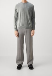 Pull en tricot gris clair à col rond et ourlet côtelé, porté avec un pantalon ample gris clair et des baskets noires.