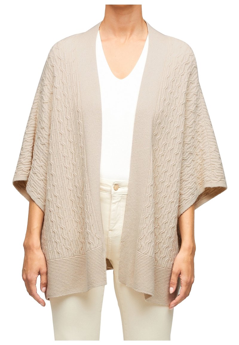 Cardigan beige lavorato a maglia con un motivo testurizzato, aperto davanti, maniche ampie e orlo a costine. Indossato sopra una maglietta bianca e pantaloni di colore chiaro.