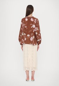 Bruine bloemenblouse met lange mouwen, gecombineerd met een crèmekleurige kant midi rok met ronde uitsparingen en een gegolfde zoom.