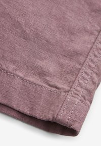 Nærbillede af mauve linnedstof, der viser detaljeret syning og kantning af en ærme eller benet på et tøj.