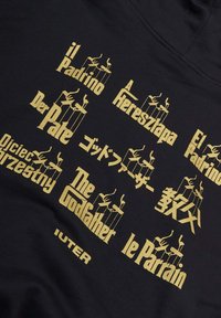 Felpa nera con testo dorato "Il Padrino" in diverse lingue e grafica di mani di burattino, con il marchio "IUTER" in basso.
