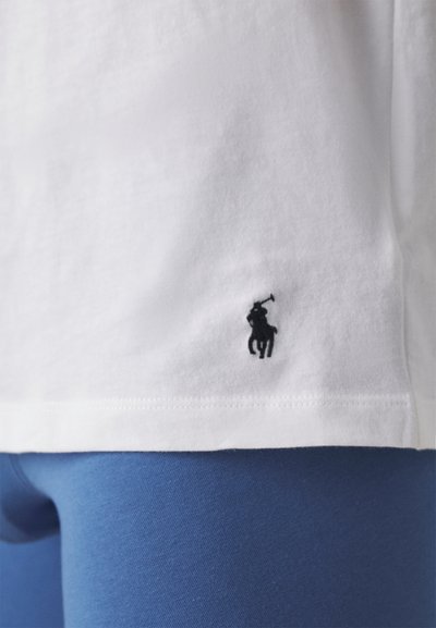 Balta medvilnės marškinėliai su juodu siuvinėtų arklių logotipu apatiniame kairiajame kampe. Jų derinys su mėlynomis tamprėmis, kurios rodo lygią tekstūrą.