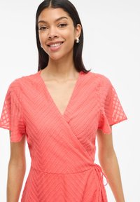 Korálové zavinovacie šaty s výstrihom do v, krátkymi rukávmi a textúrovaným zigzag vzorom. Ľahký materiál s viazacím pásom v oblasti pása.