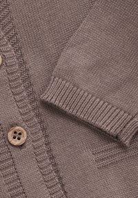Brun strik cardigan med ribbede manchetter og en tekstureret front. Har en stor træknap til lukning og synlige syninger.