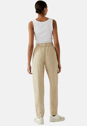 Linnen broeken in een lichte beige kleur met een relaxte pasvorm, elastische tailleband en twee achterzakken, gecombineerd met een witte tanktop en sneakers.