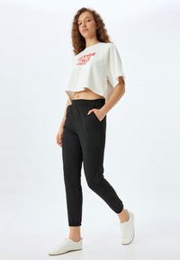 Camiseta corta blanca con texto rojo, combinada con pantalones de cintura elástica negros y zapatillas blancas. Tela suave y diseño de corte holgado.