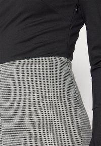 Gros plan d'un haut noir à manches longues associé à une jupe taille haute noire et blanche à motif pied-de-poule.