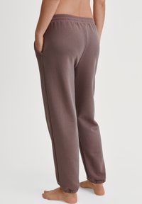 Weiche, gerippte, braune Sweatpants mit einem elastischen Bund, Seitentaschen und Bündchen an den Knöcheln, die eine lässige Passform und eine glatte Textur aufweisen.