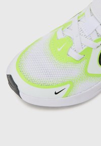 Chaussure de sport blanche avec des accents vert vif, dessus en mesh et logo Nike noir. Présente des détails réfléchissants et une semelle en caoutchouc durable.