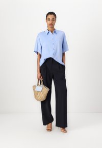 Light blue short-sleeved button-up shirt, black wide-leg trousers, and a woven straw handbag with blue accents. Sandals complete the look.