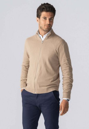 Kaki zip-sweater i et glat strikstof, med ribkant ved kraven og ærmerne, parret med navy bukser. Enkel, ren design.