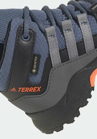 Hikingová obuv Adidas Terrex s šedou a námořnickou síťovinou, zesílenou patou, logem Gore-Tex a strukturovanou gumovou podrážkou pro trakci.