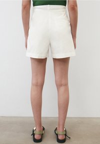 White shorts with a smooth texture, high waist, and rolled cuffs; worn with black sandals featuring green straps. Back view displayed.
