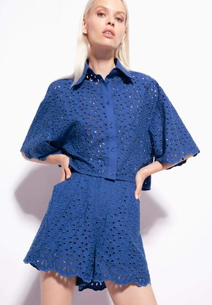 Chemise bleue à manches courtes et shorts assortis en tissu brodé avec des motifs de feuilles. Comprend un devant à boutons et des bords festonnés.