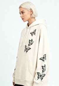 Felpa con cappuccio beige con ricamo di farfalle nere sulla parte anteriore e sulle maniche, dotata di tasca frontale e cappuccio con coulisse. Texture morbida.